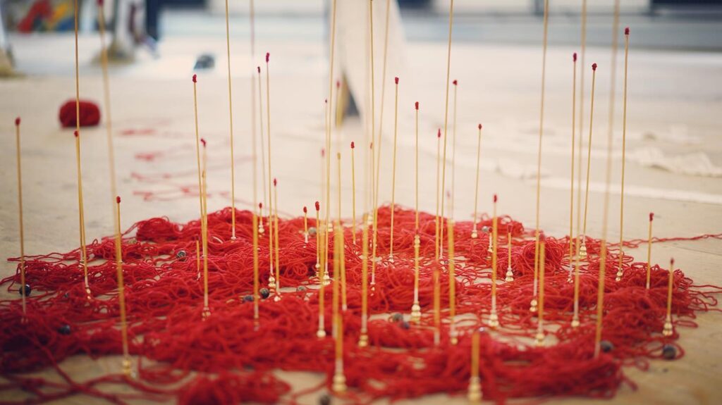 Floor installation made from red thread and many thin upright rods