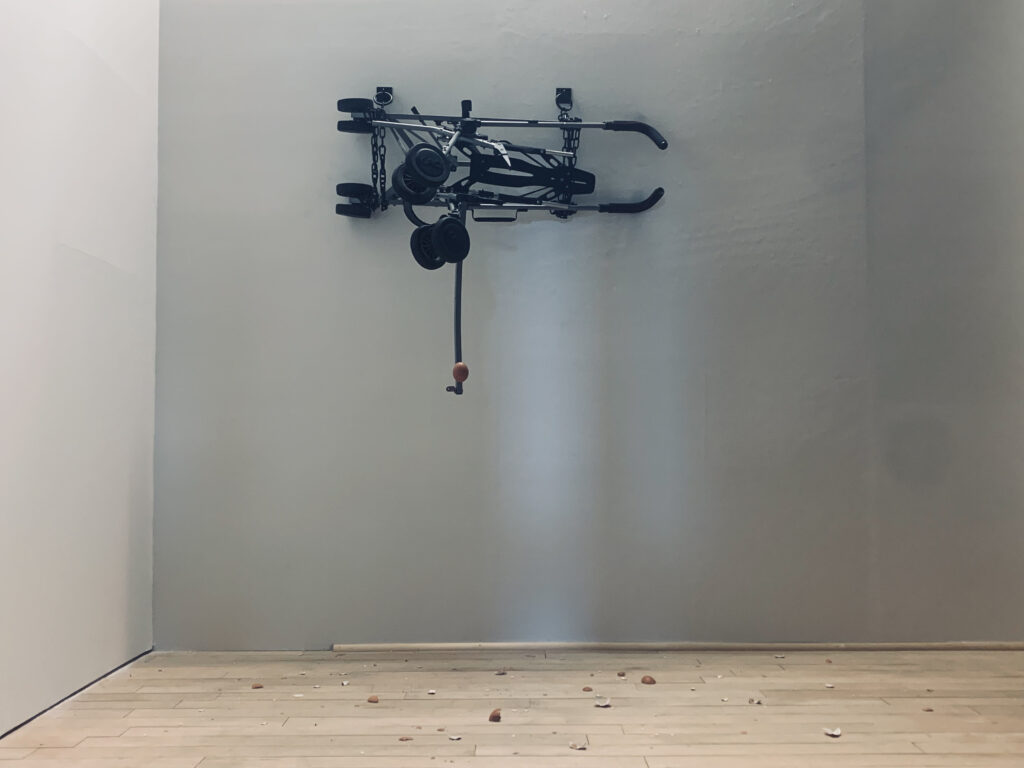 Black folded trolley mounted high on a gallery wall above scattered objects